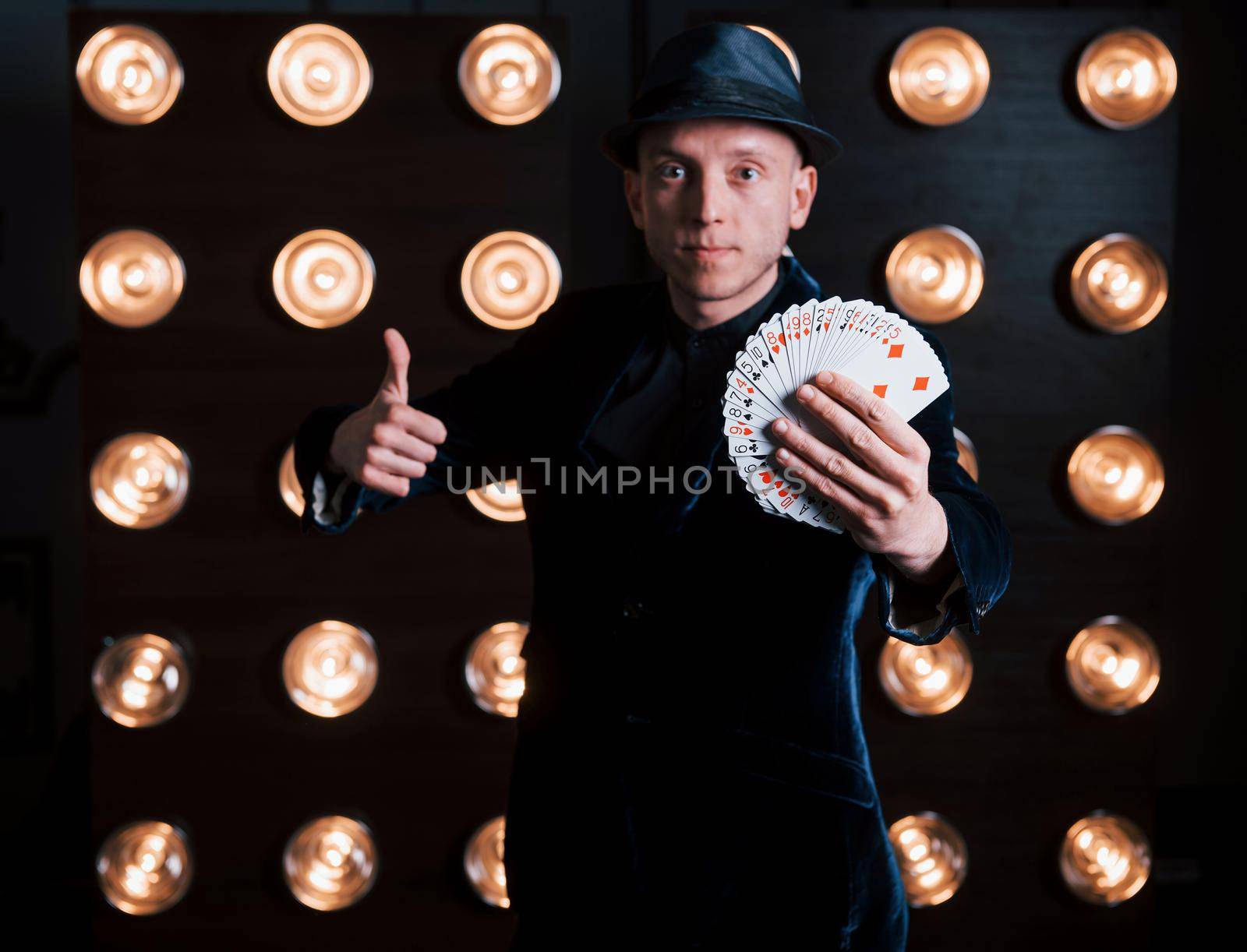 Magician in black suit standing in the room with special lighting at backstage.