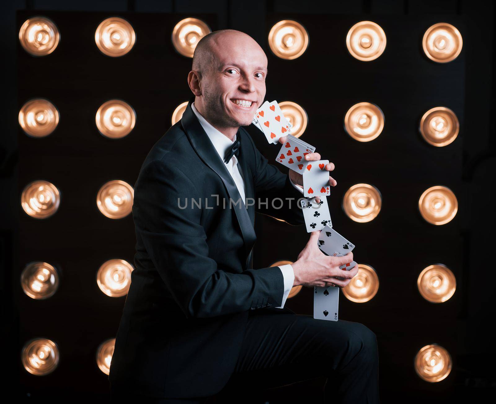 In love with his job. Magician in black suit and with playing cards standing in the room with special lighting at backstage.