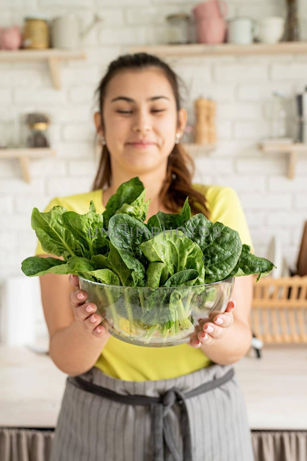 Preparing healthy foods. Healthy eating and dieting. Young caucasian brunette woman holding a bowl of fresh spinach in the kitchen