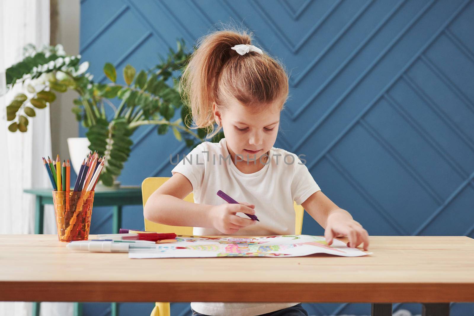 Front view. Cute little girl in art school draws her first paintings by pencils and markers.