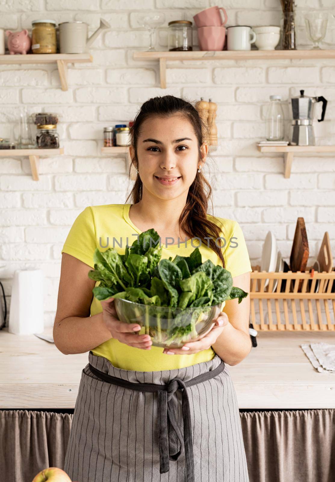 Preparing healthy foods. Healthy eating and dieting. Young caucasian brunette woman holding a bowl of fresh spinach in the kitchen