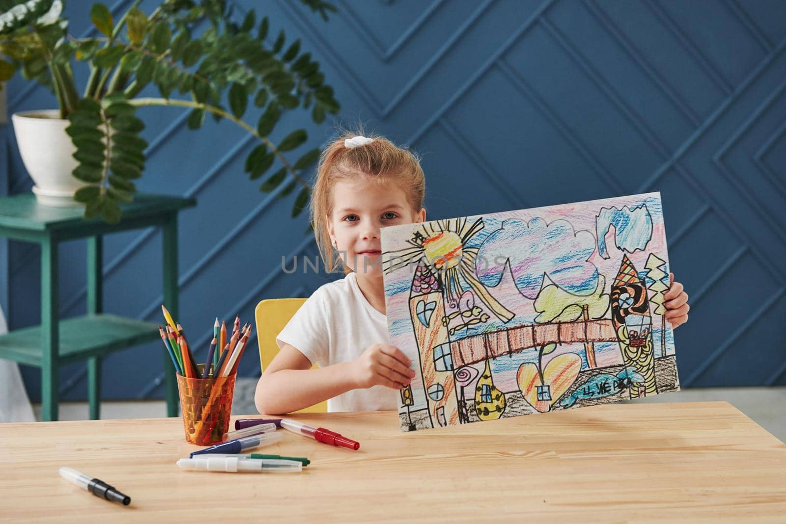 Nice interior in the room. Cute little girl in art school shows her first paintings drawn by pencils and markers.