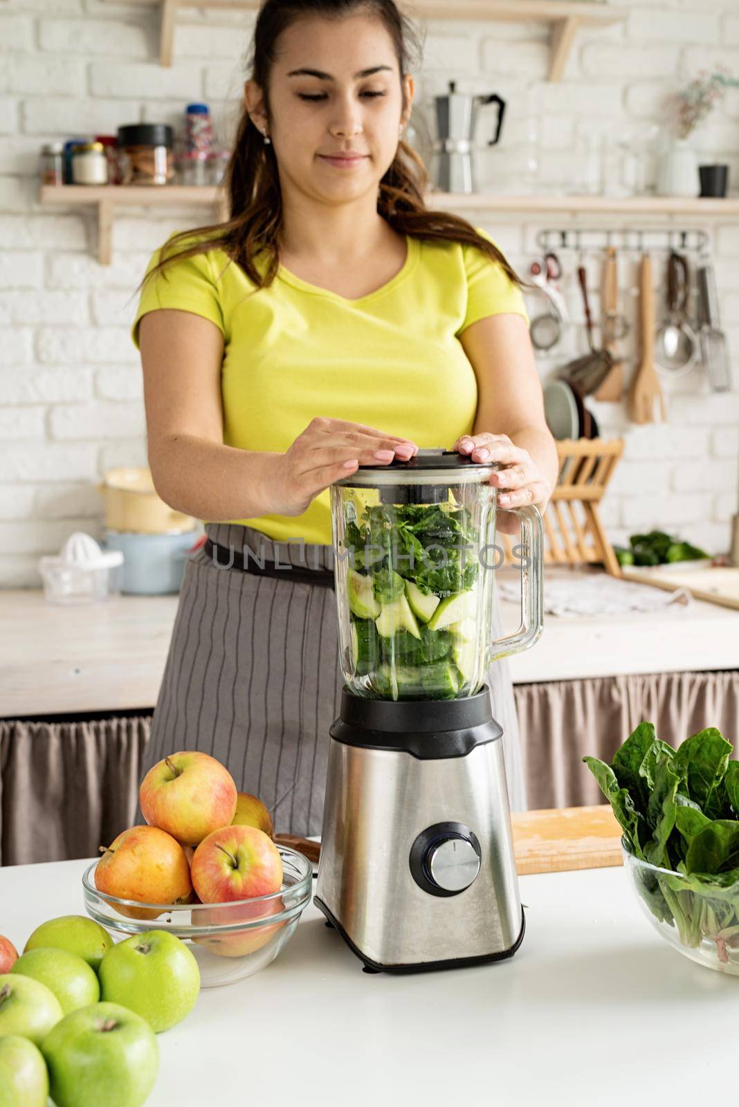 Preparing healthy foods. Healthy eating and dieting. Young brunette woman making green smoothie at home kitchen