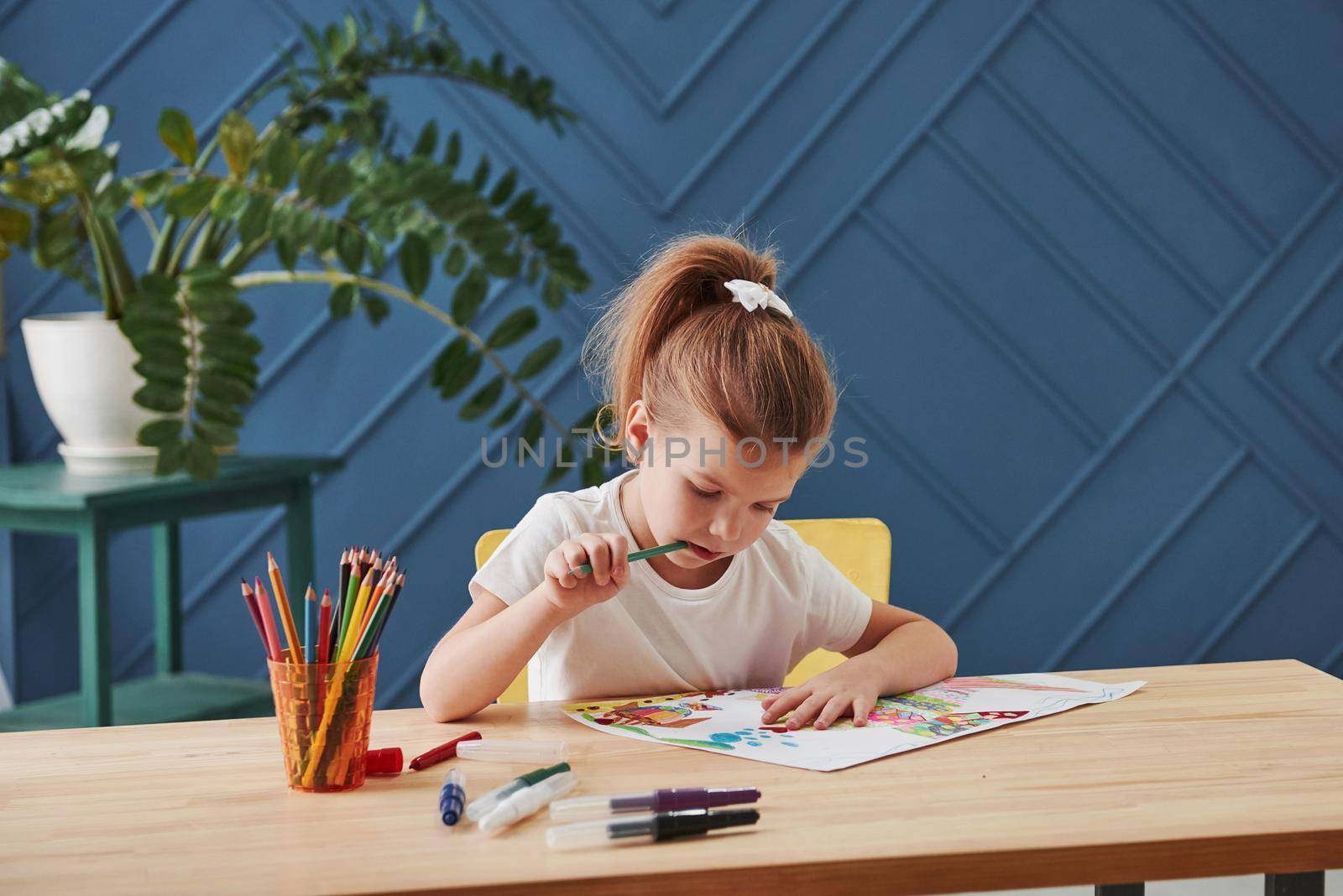 Thinks about what to add. Cute little girl in art school draws her first paintings by pencils and markers.