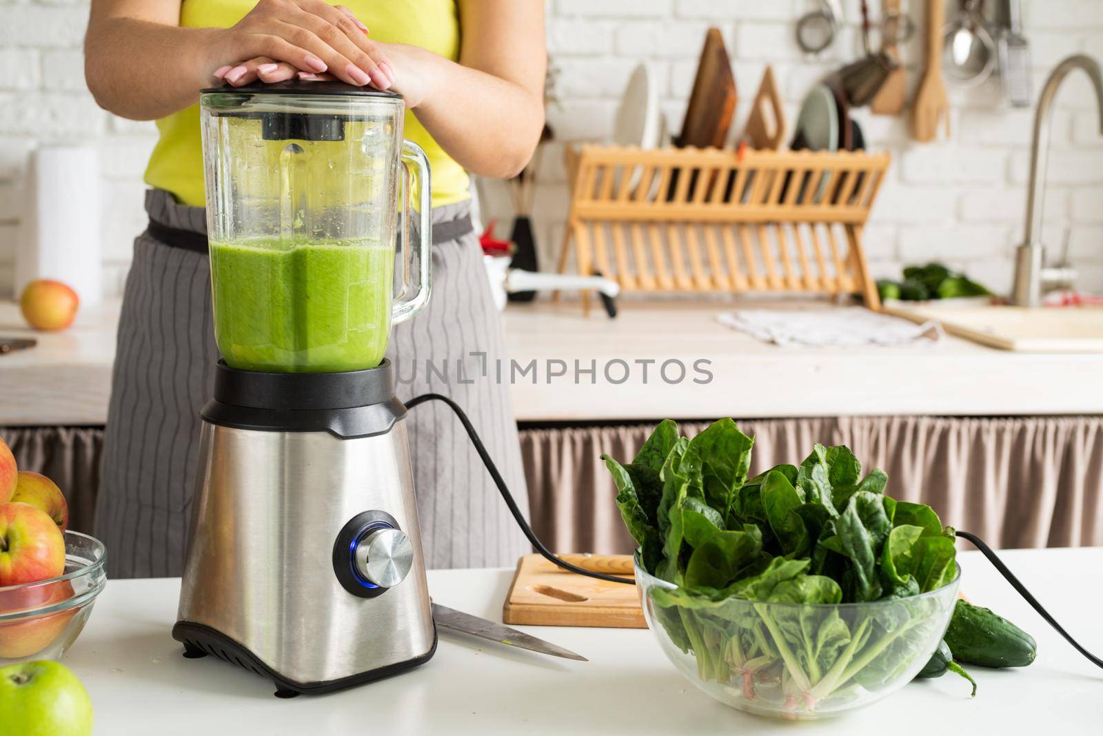 Young woman making green smoothie at home kitchen by Desperada