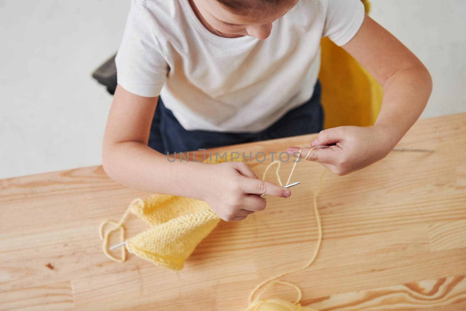 Everything going good. Kid is knitting at home. Cute little girl sitting near the wooden table is learning some new stuff.