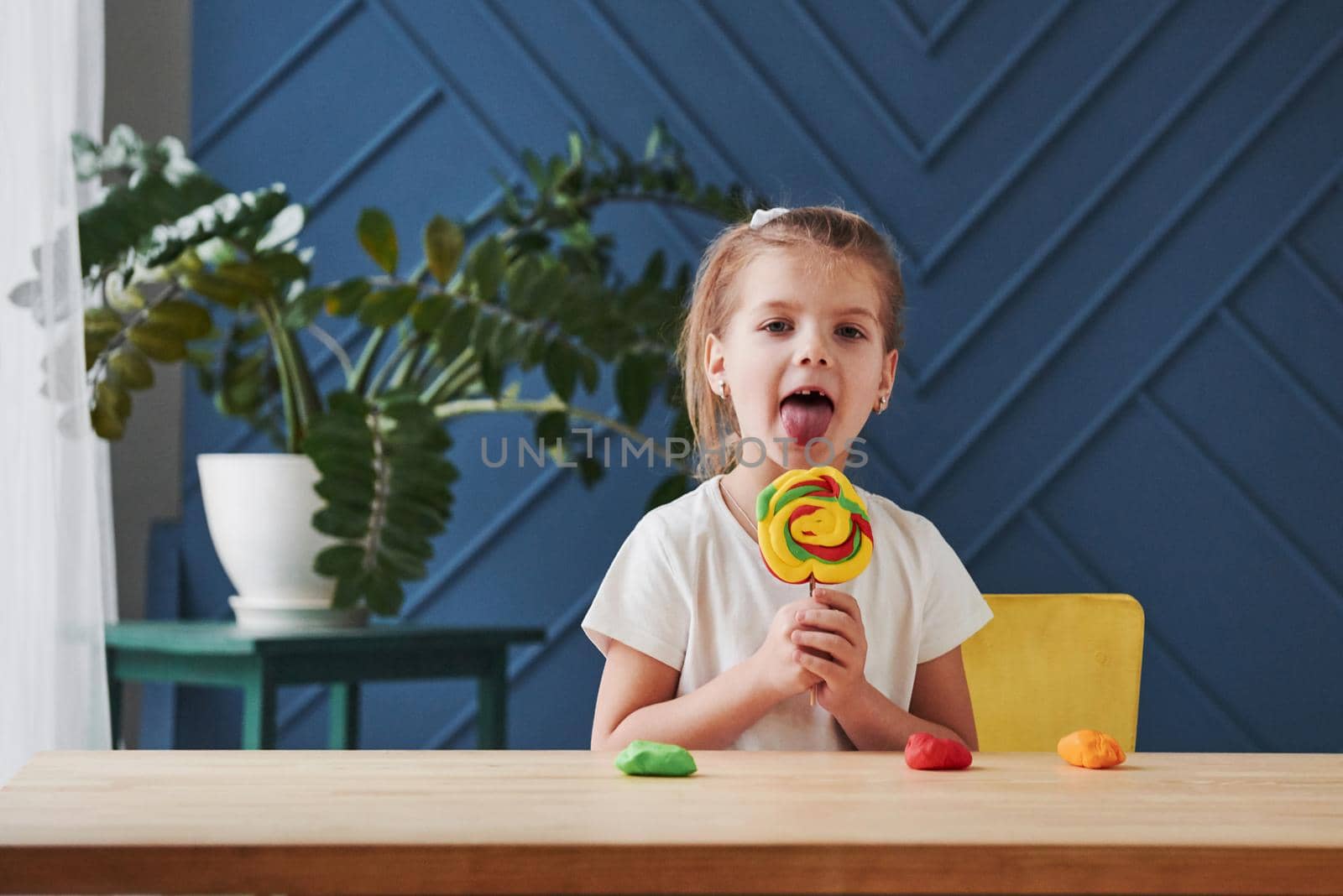 Shows her crafted candy. Children playing with colored plasticine on the wooden table at home.