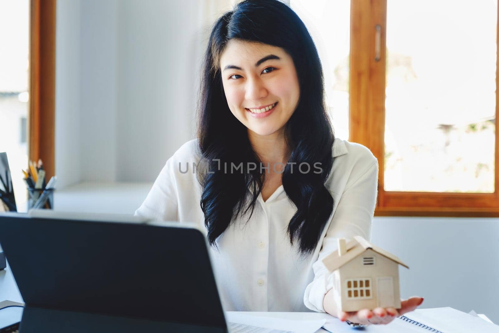 Accountant, businessman, real estate agent, Asian business woman handing model house to customers along with house interest calculation documents for customers to sign