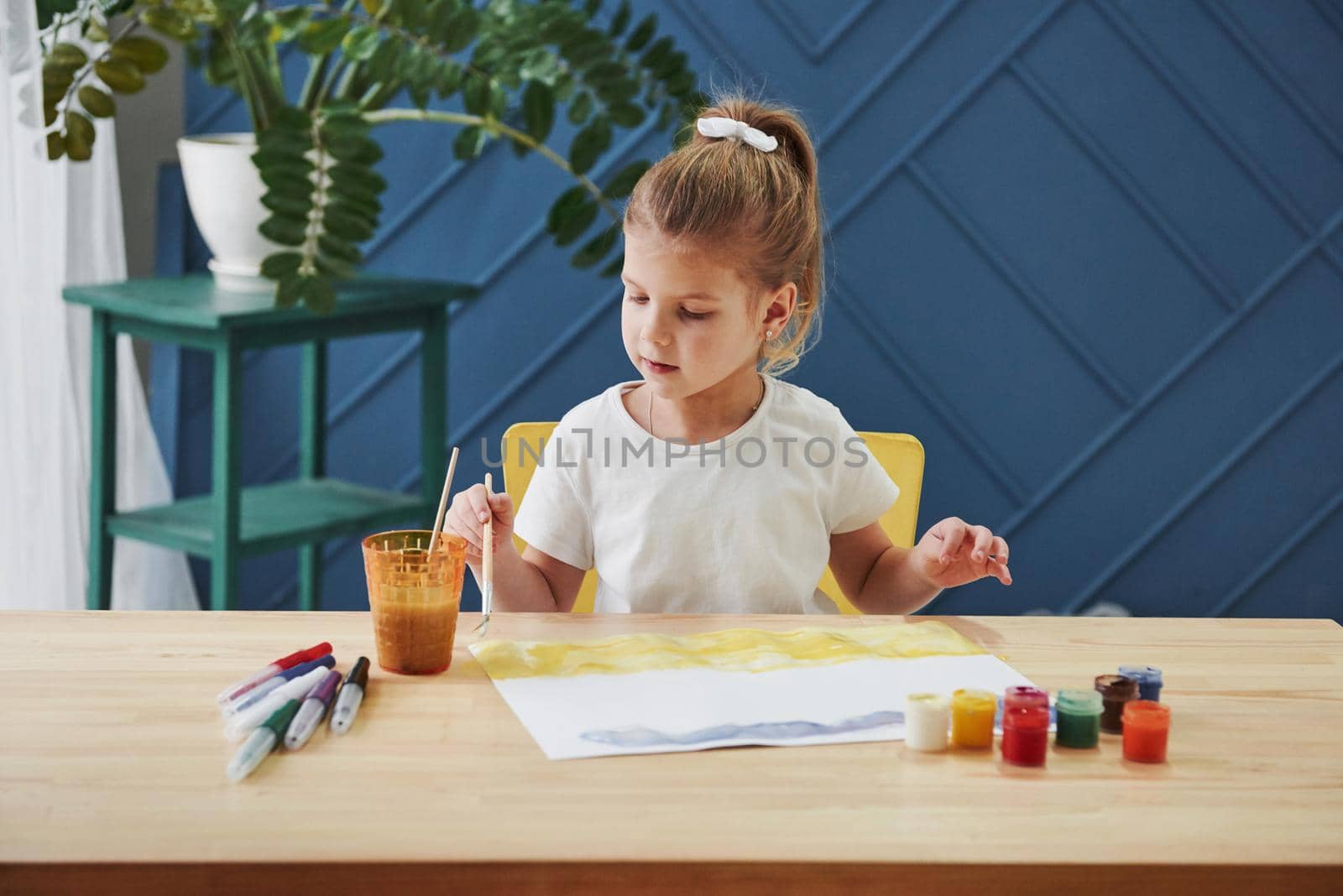 Variety of colours. Little girl is drawing by using gouache and brush. Learning in the art class.