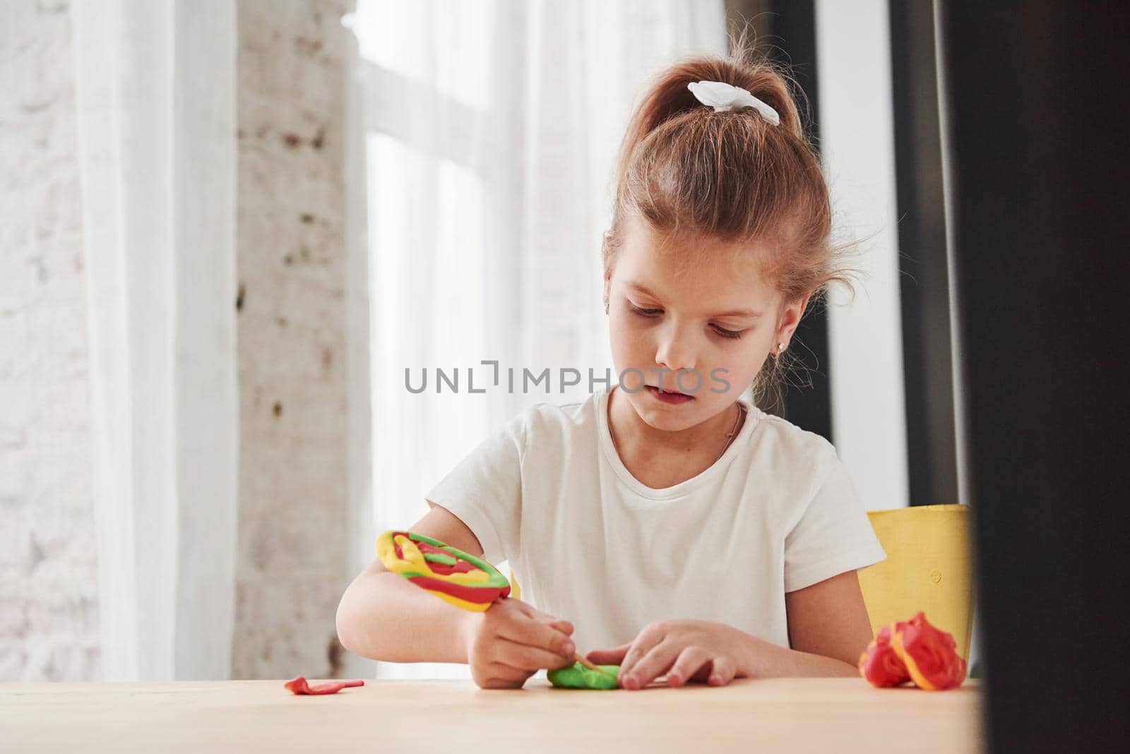 Using stick from artificial candy to make some new stuff. Children playing with colored plasticine on the wooden table at home.