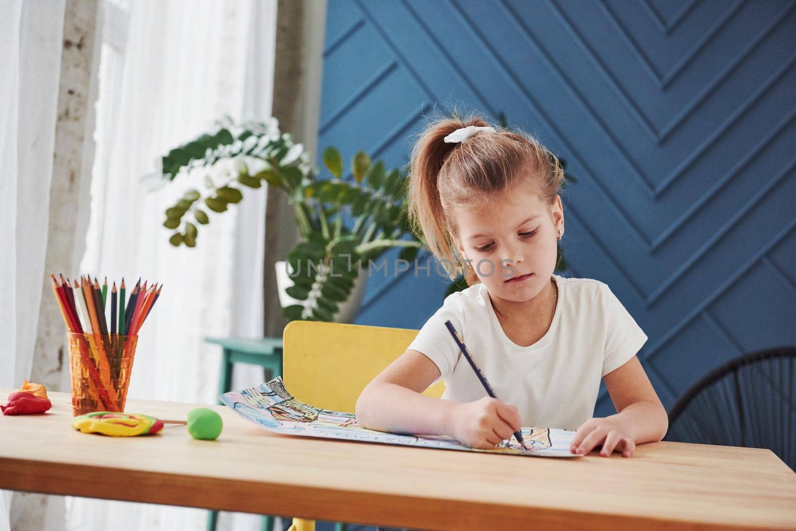 Good interior at daytime. Cute little girl in art school draws her first paintings by pencils and markers.