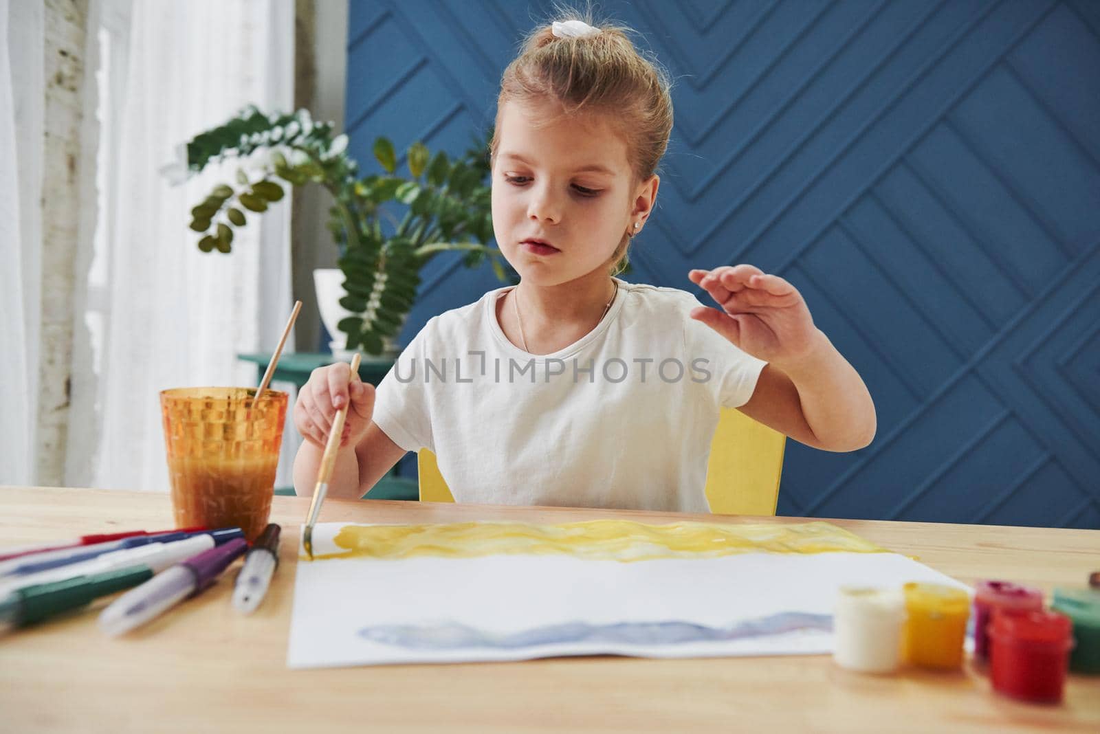 Careful movements. Little girl is drawing by using gouache and brush. Learning in the art class.