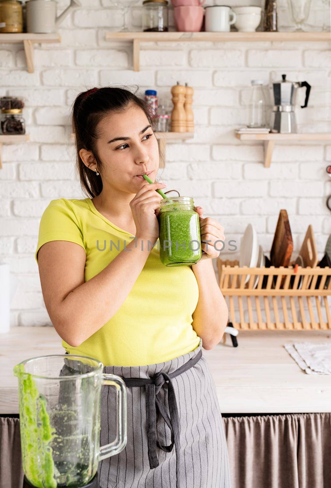 Healthy eating, dieting concept. Young brunette woman drinking green smoothie at home kitchen from mason jar