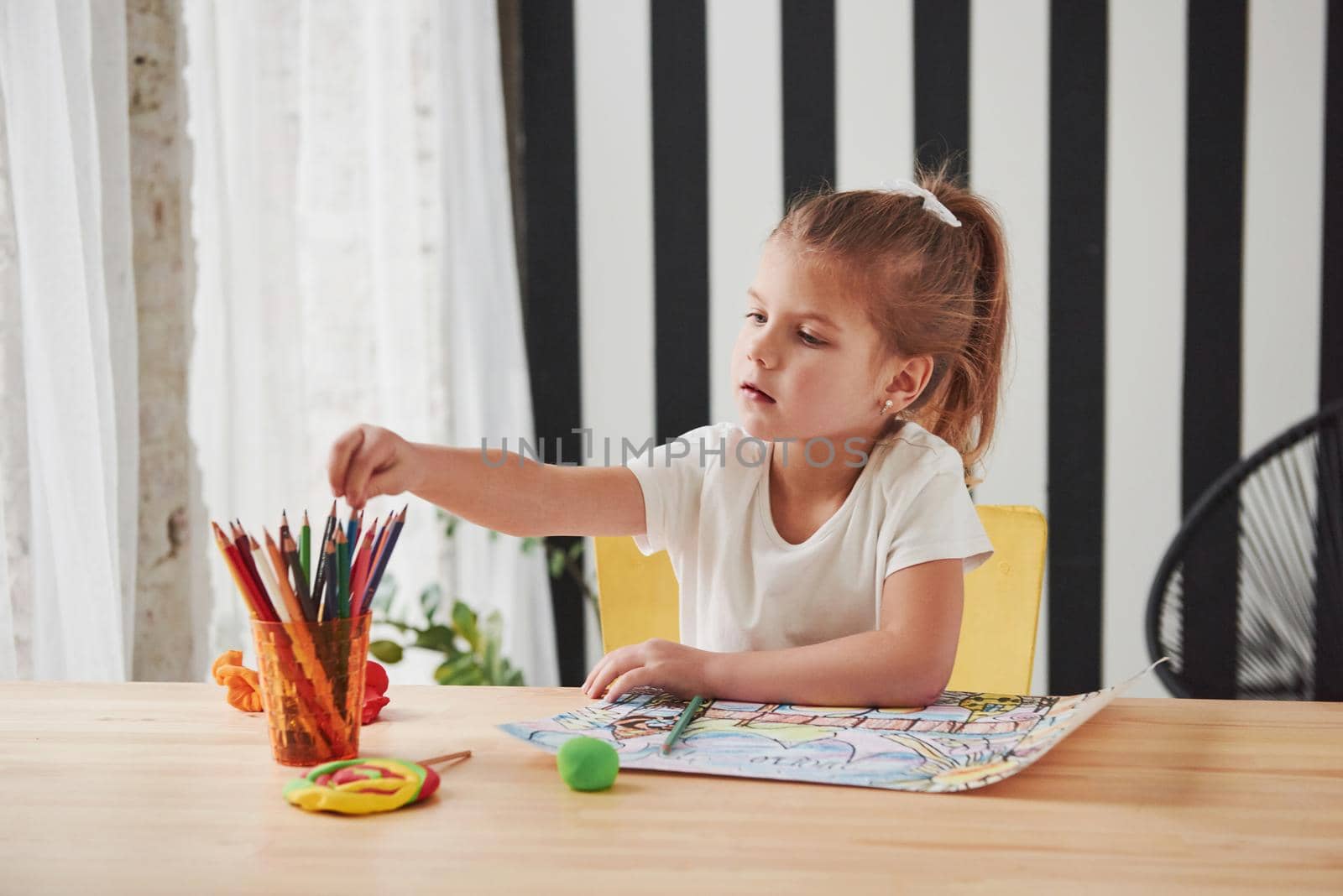 Tking the pencil. Cute little girl in art school draws her first paintings.