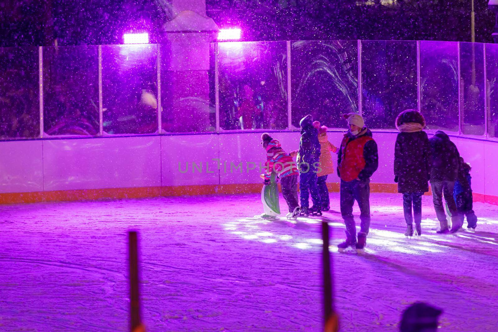 People skate in the evening on a lighted ice rink. A blizzard is raging and snow is falling. Zelenograd, Russia 28.01.2022.