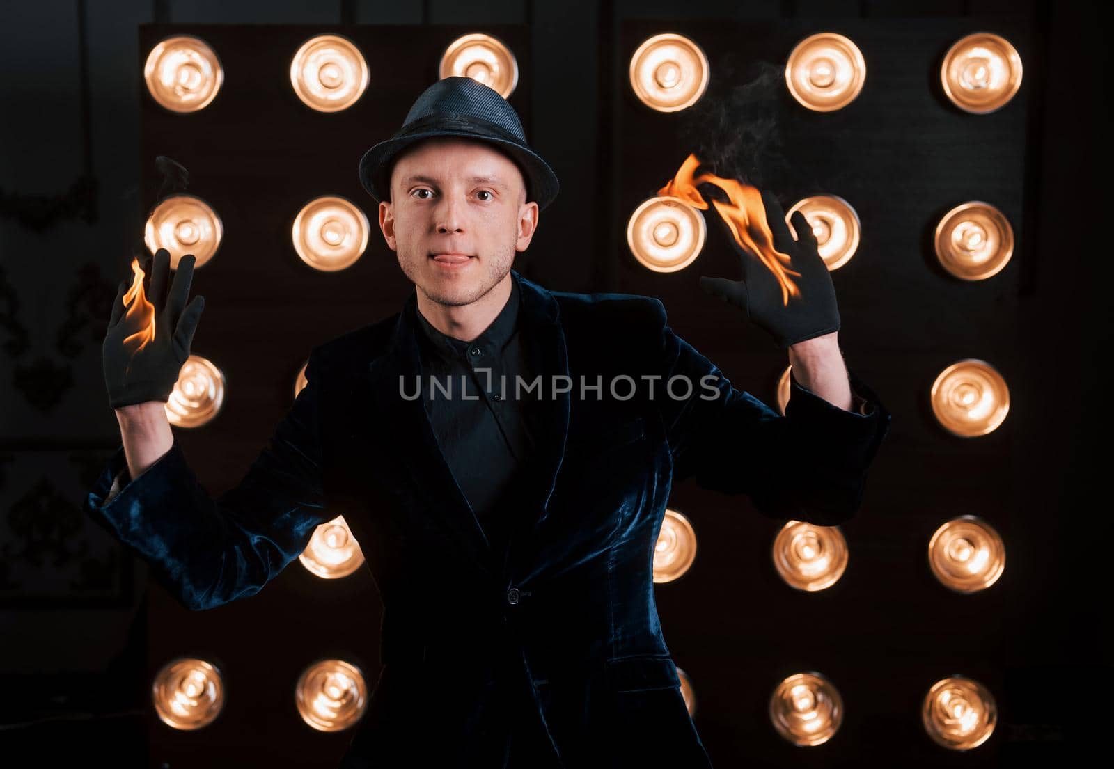 Front view. Professional illusionist in black hat, shirt and gloves playing with fire.