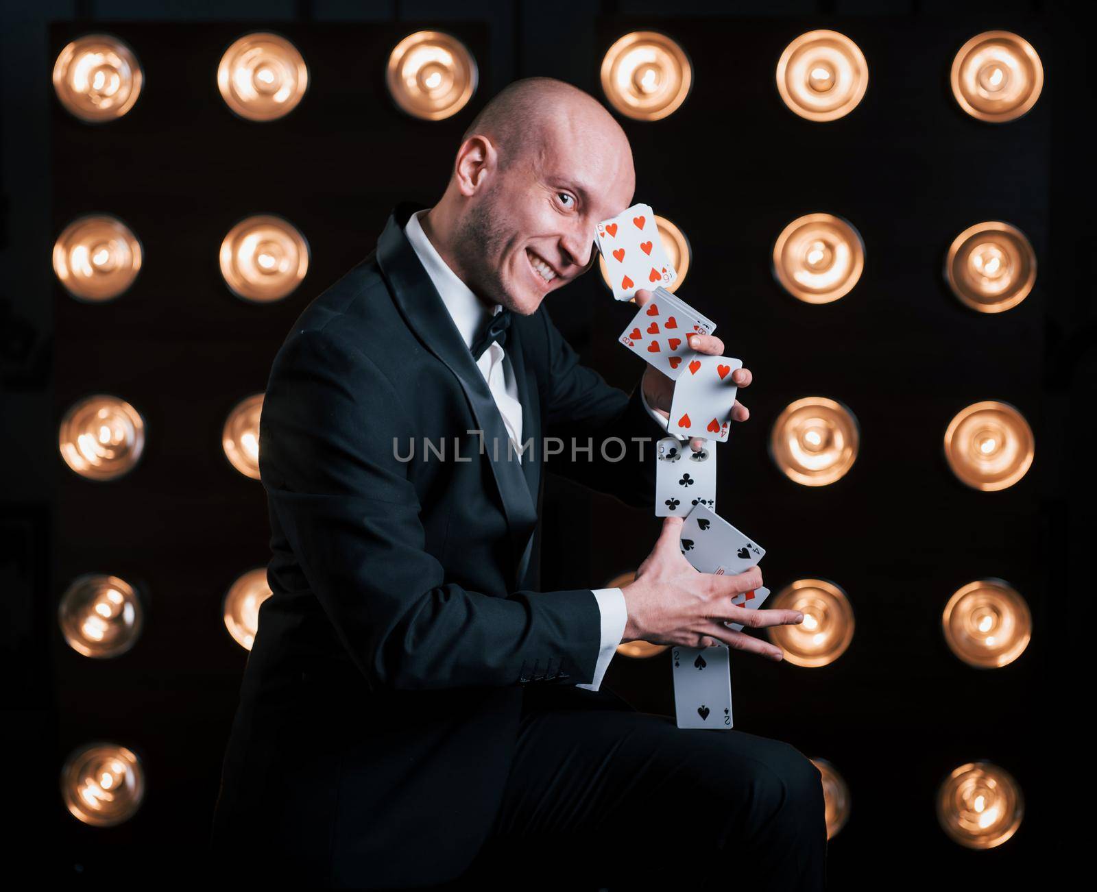 This will impress you. Magician in black suit and with playing cards standing in the room with special lighting at backstage.