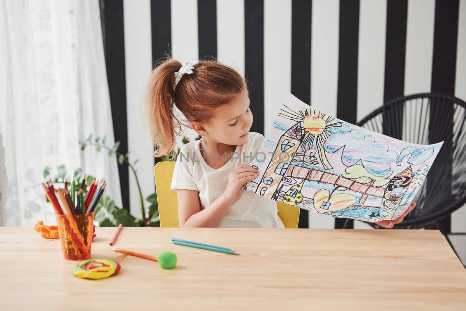 Many colorful pencils was used for this work. Cute little girl in art school shows her first paintings.