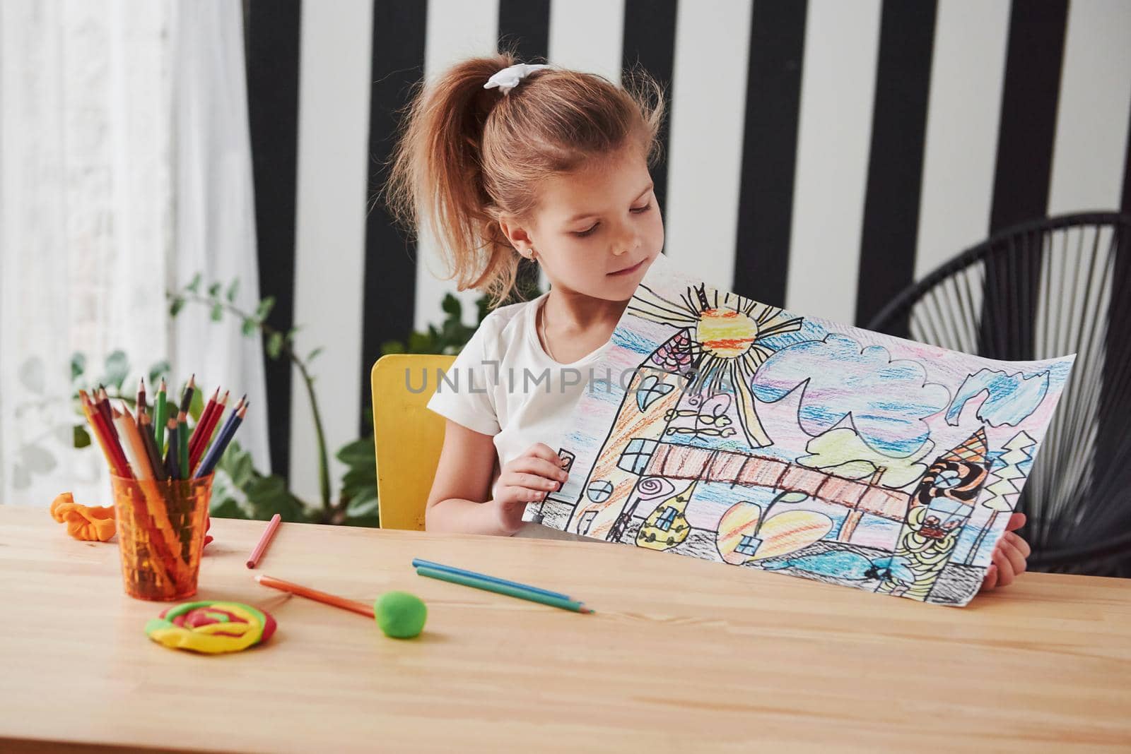 She will be professional painter one day. Cute little girl in art school shows her first picture drawn by pencils and markers.