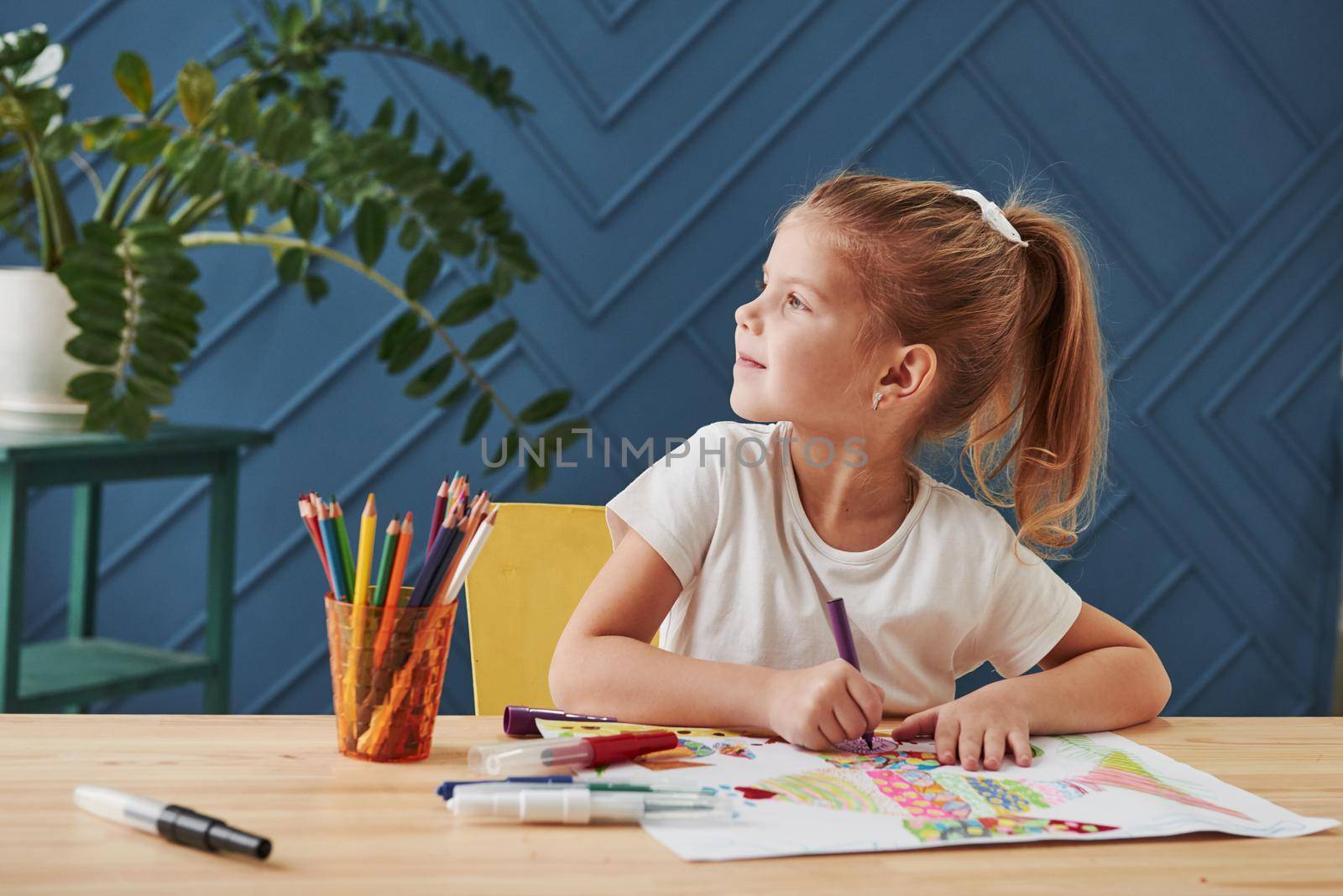 Looking to the side. Cute little girl in art school draws her first paintings by pencils and markers.