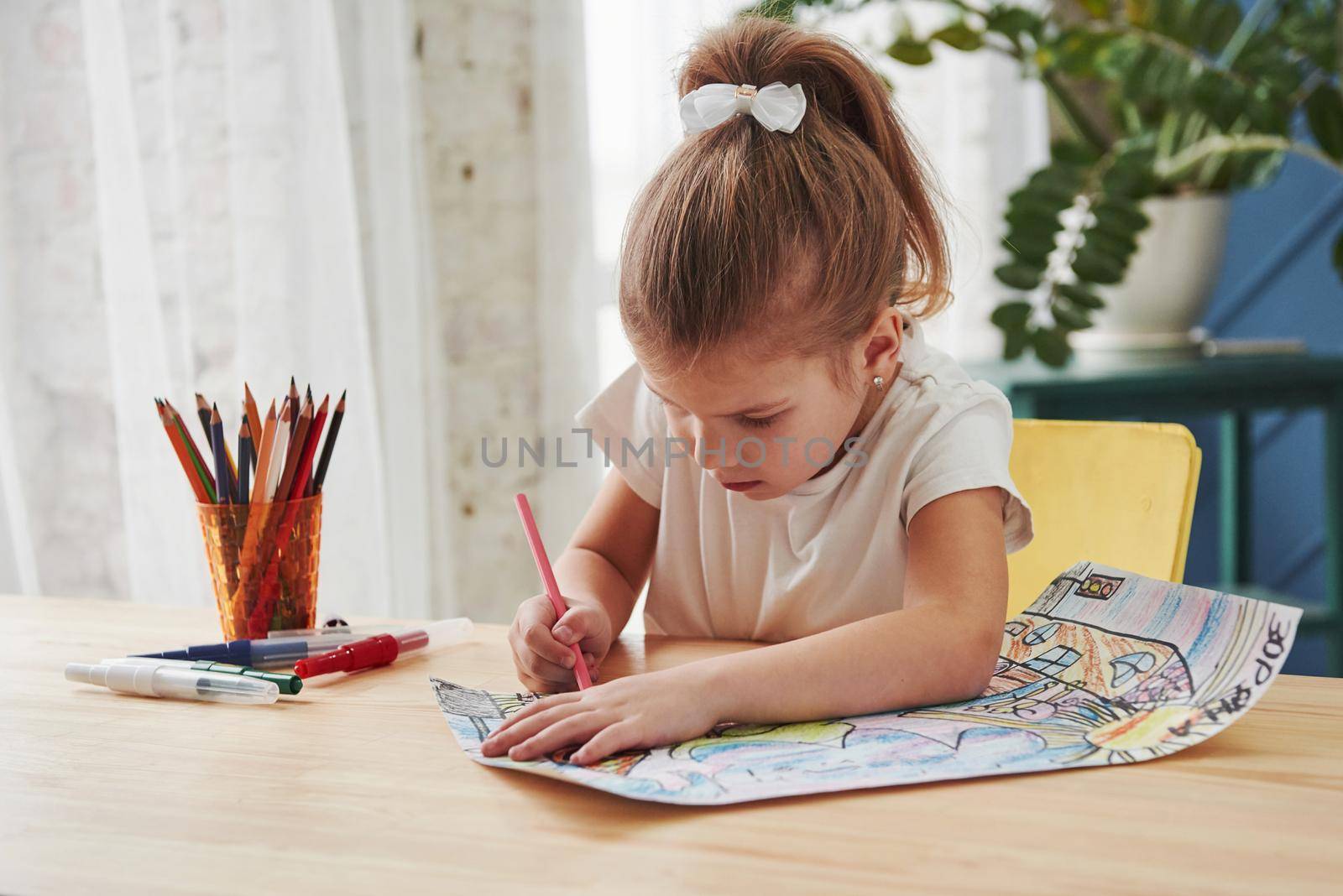 Diligent student. Cute little girl in art school draws her first paintings by pencils and markers.