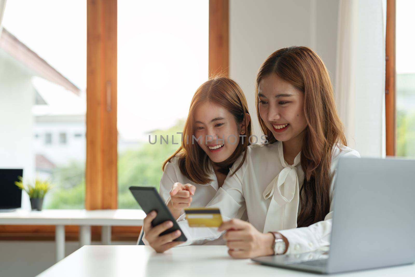 Two asian girlfriends shopping online with smart phone and credit card at home