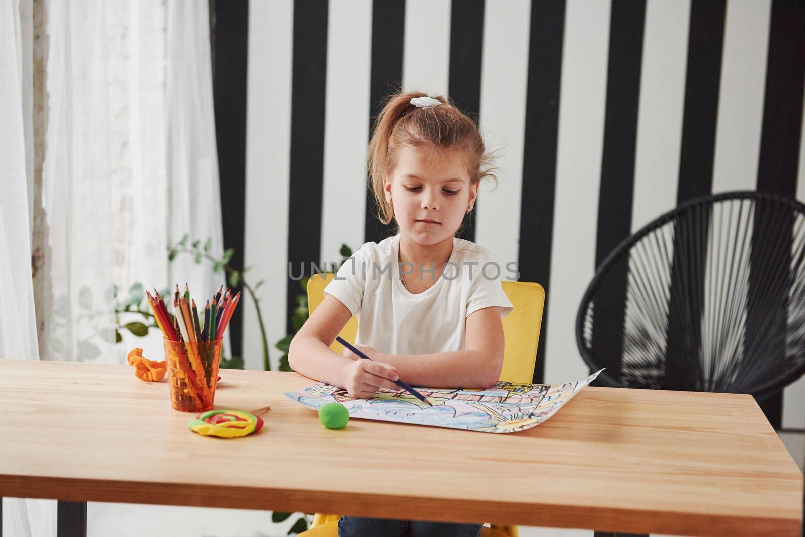 Serious look. Cute little girl in art school draws her first paintings by pencils and markers.