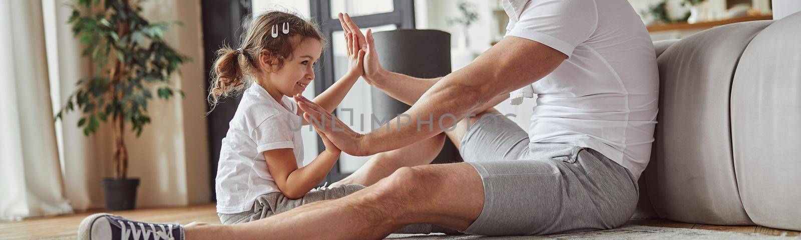 Low angle of merry man and little girl during hands-up game in cozy living room