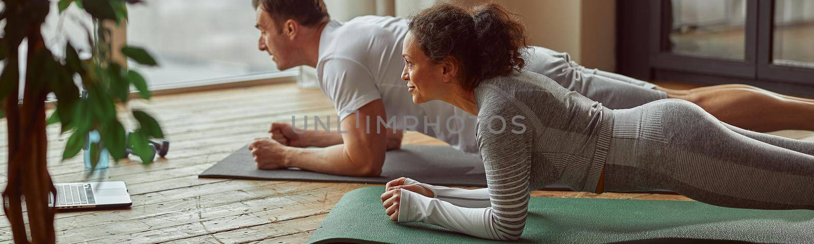 Sporty couple doing plank before laptop indoors by Yaroslav_astakhov
