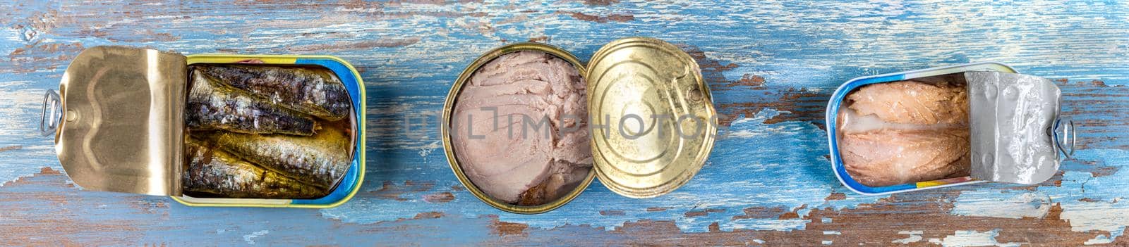 Panoramic image, Various canned fish and seafood in a metal cans. Wooden blue background. Top view by JPC-PROD