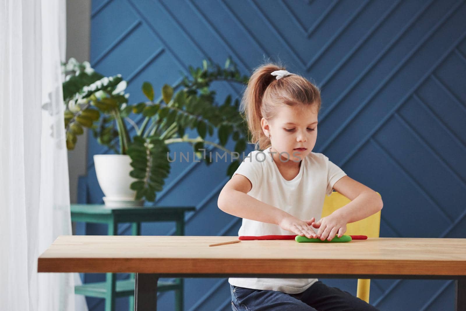 Children playing with colored plasticine on the wooden table at home.