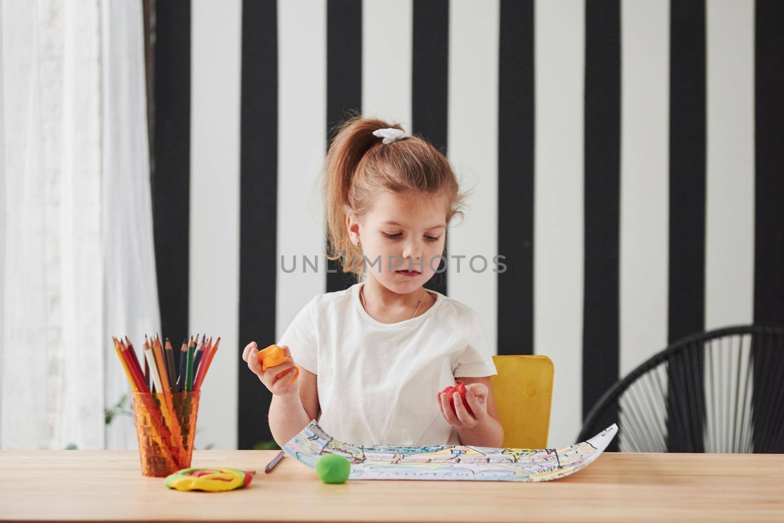 Holds plasticine. Cute little girl in art school draws her first paintings by pencils and markers.