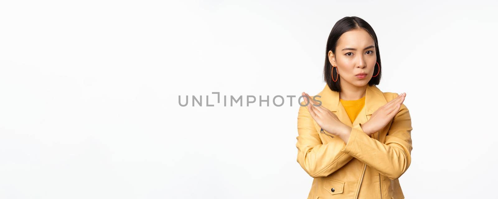Stop gesture. Serious asian woman making arm cross, prohibit smth, rejecting, dislike and disapprove action, standing over white background.