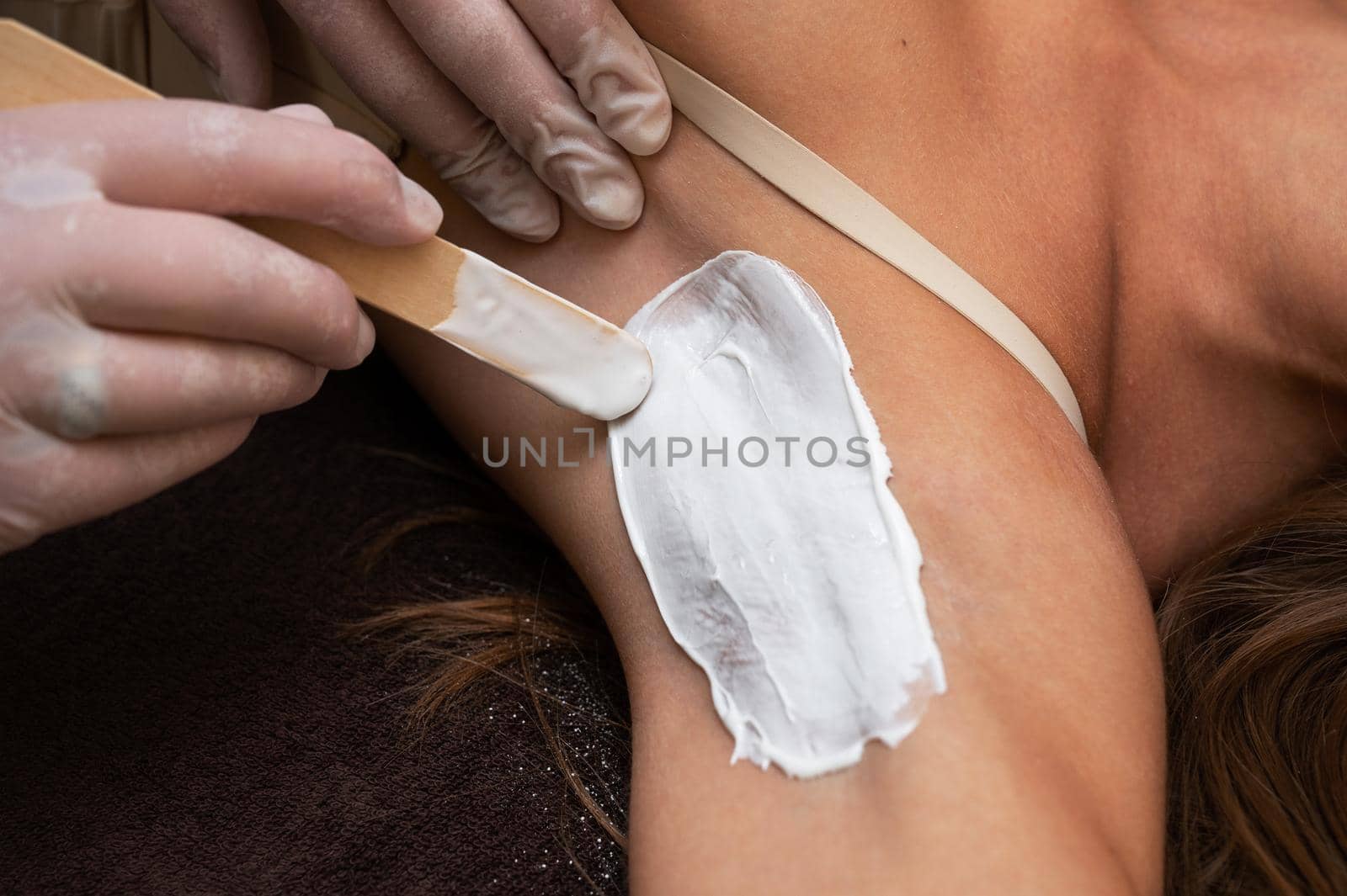 Cosmetologist in beauty clinic performs a epilation procedure for removing hair from the armpits using a white shugaring paste. Beauty and body care concept.