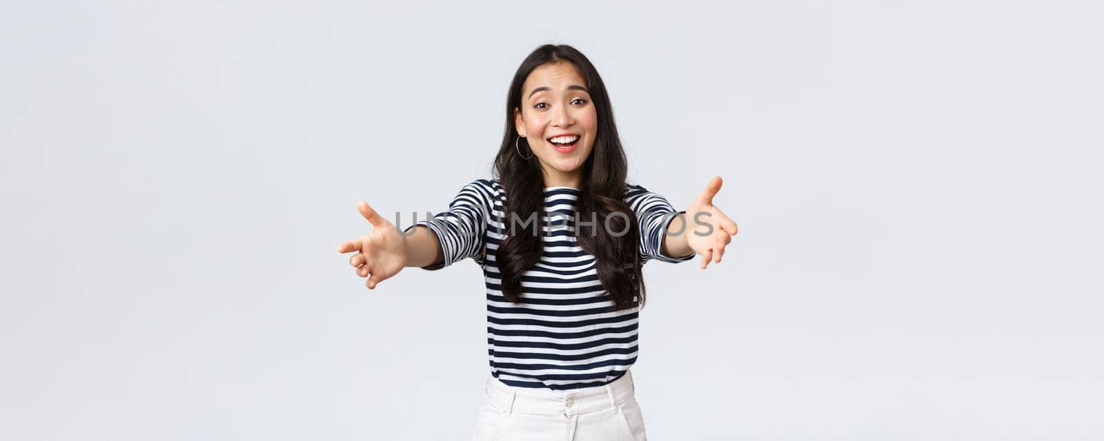 Lifestyle, people emotions and casual concept. Friendly charming asian girl reaching hands forward to hold something, giving hug or embracing, standing white background.