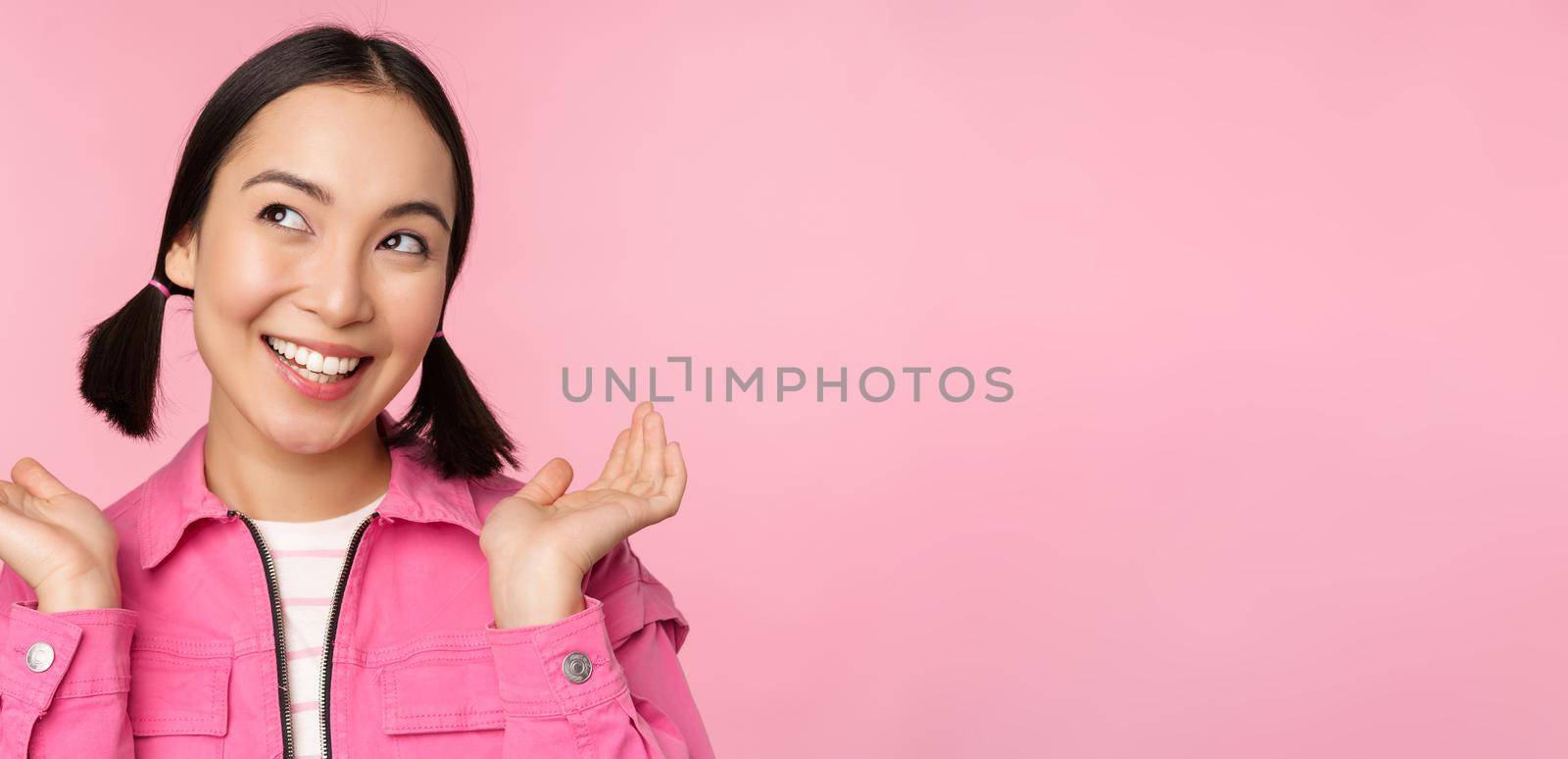 Skin care and cosmetology concept. Beautiful asian girl smiling and laughing, showing clean healthy facial skin, posing against pink background. Copy space