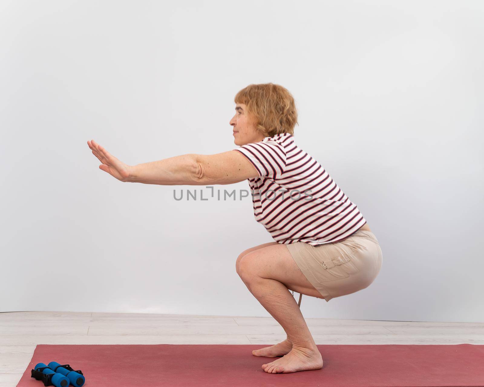 Elderly woman doing squats on a white background. The old lady is doing exercises for her health.