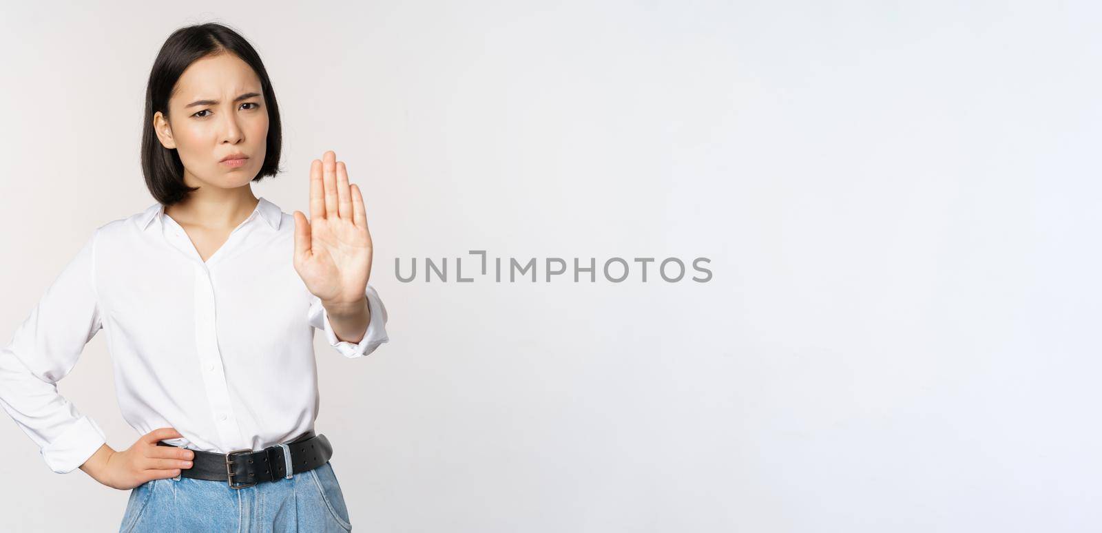Portrait of young woman extending one hand, stop taboo sign, rejecting, declining something, standing over white background. Copy space