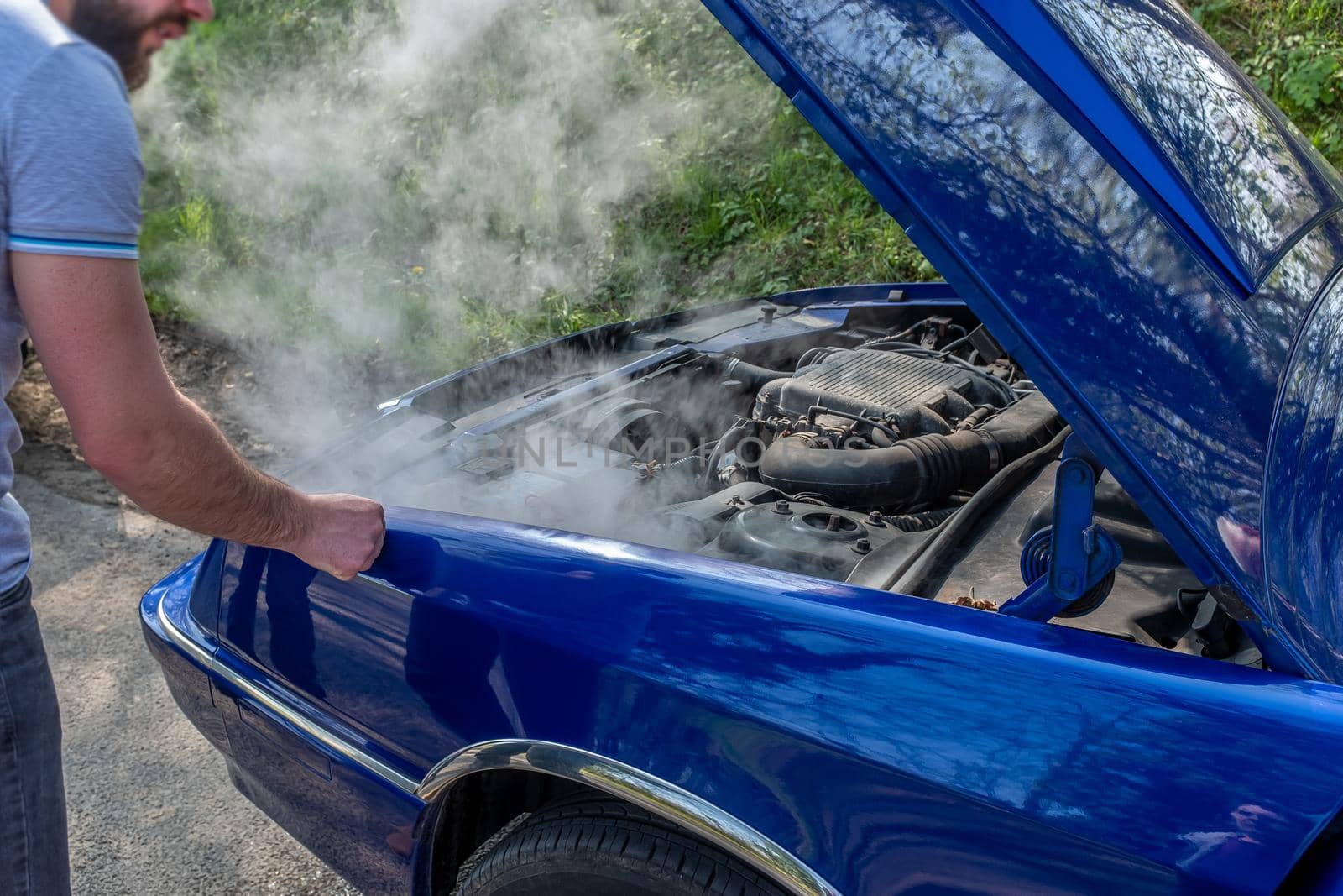 Car, open hood giving off white smoke on the side of the road.