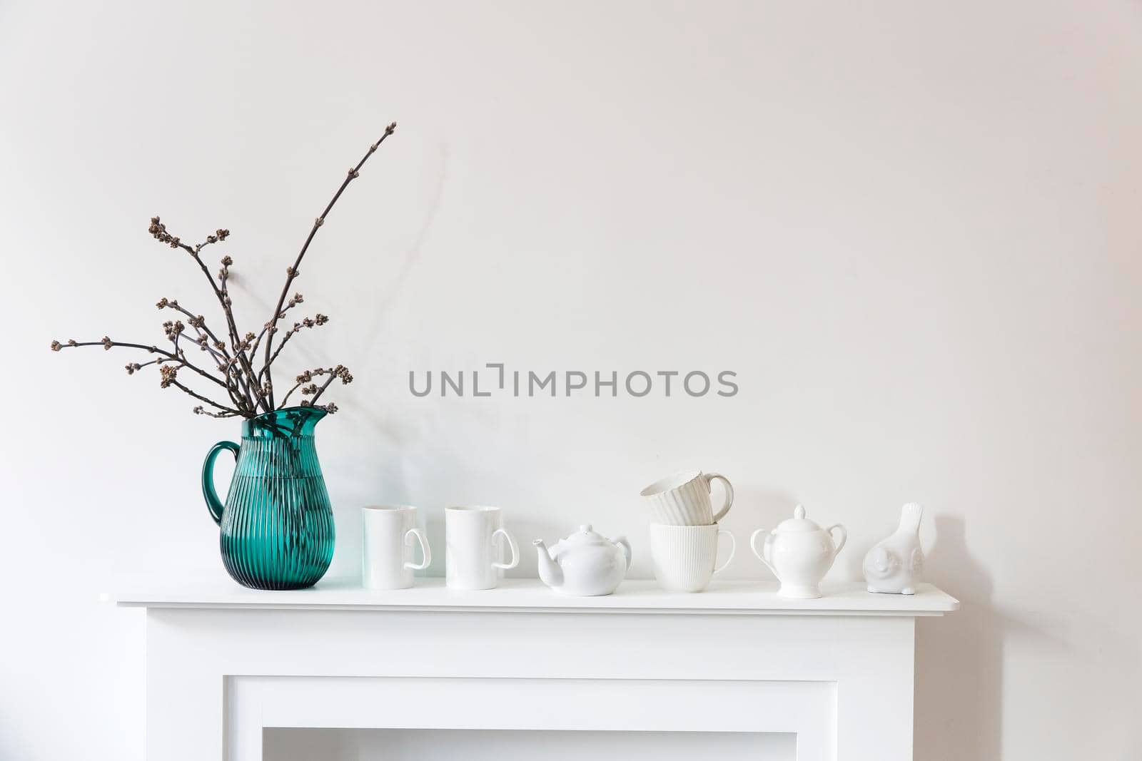 American maple branches in a green glass jar, porcelain cups, figurines, teapot on a white chest of drawers. Scandinavian style