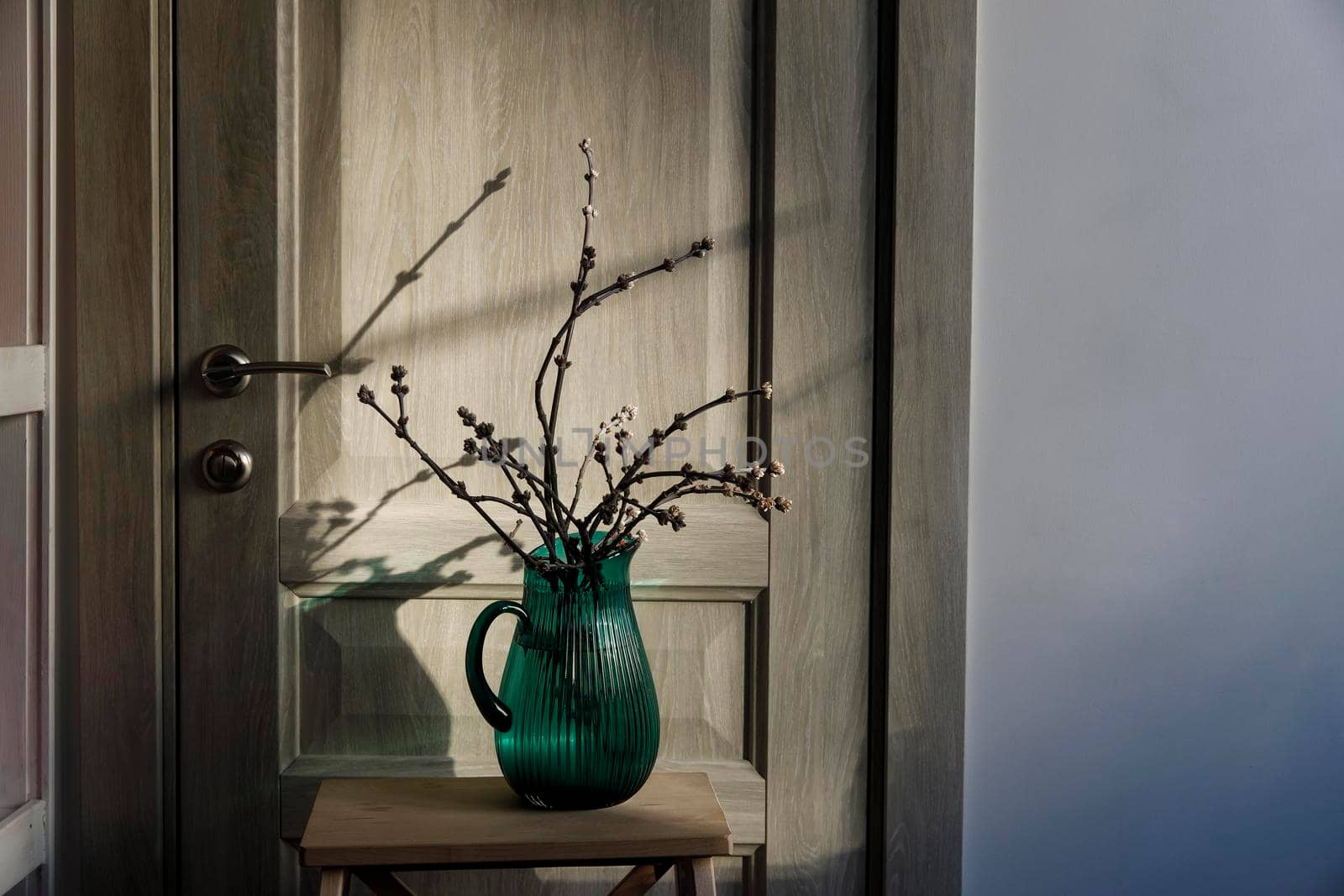 Cut branches of an apple tree in a green jug on a beige table in the kitchen