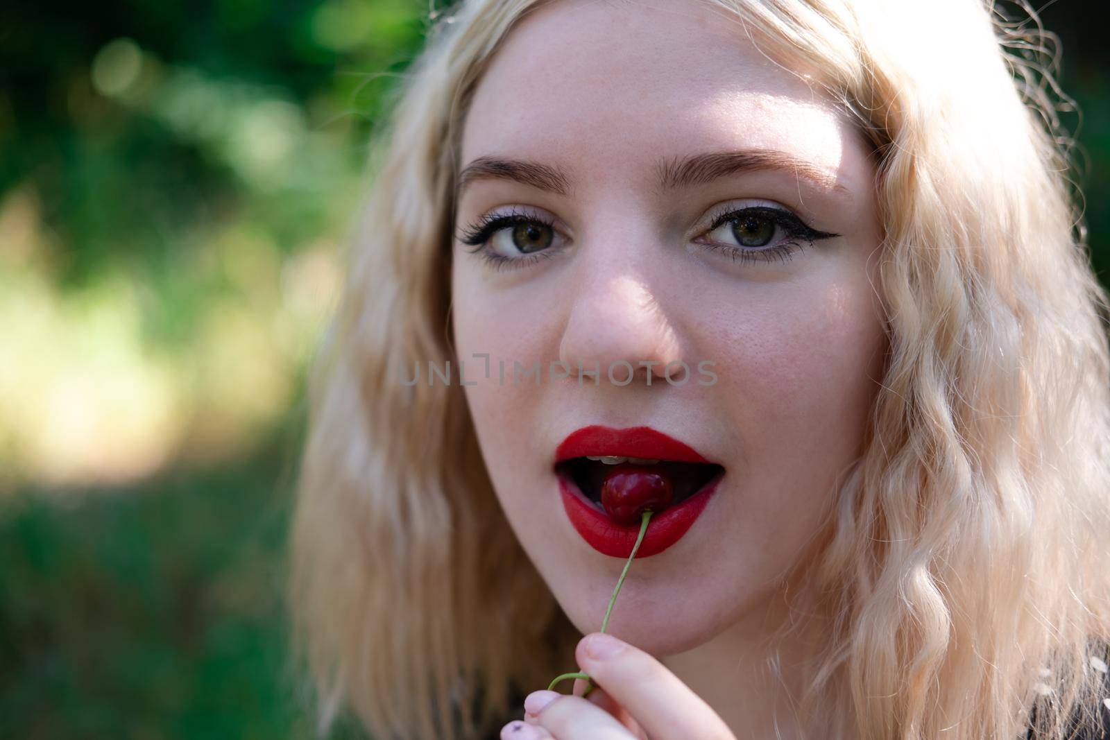portrait of a charming blonde teenage girl wearing teeth braces biting a sweet cherry.