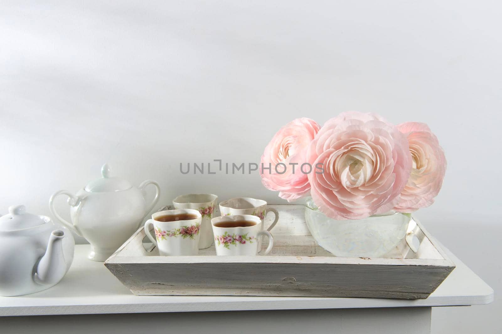 Three pale pink ranunculus in a transparent round vase on the white windowsill. Copy space. Place for text by elenarostunova