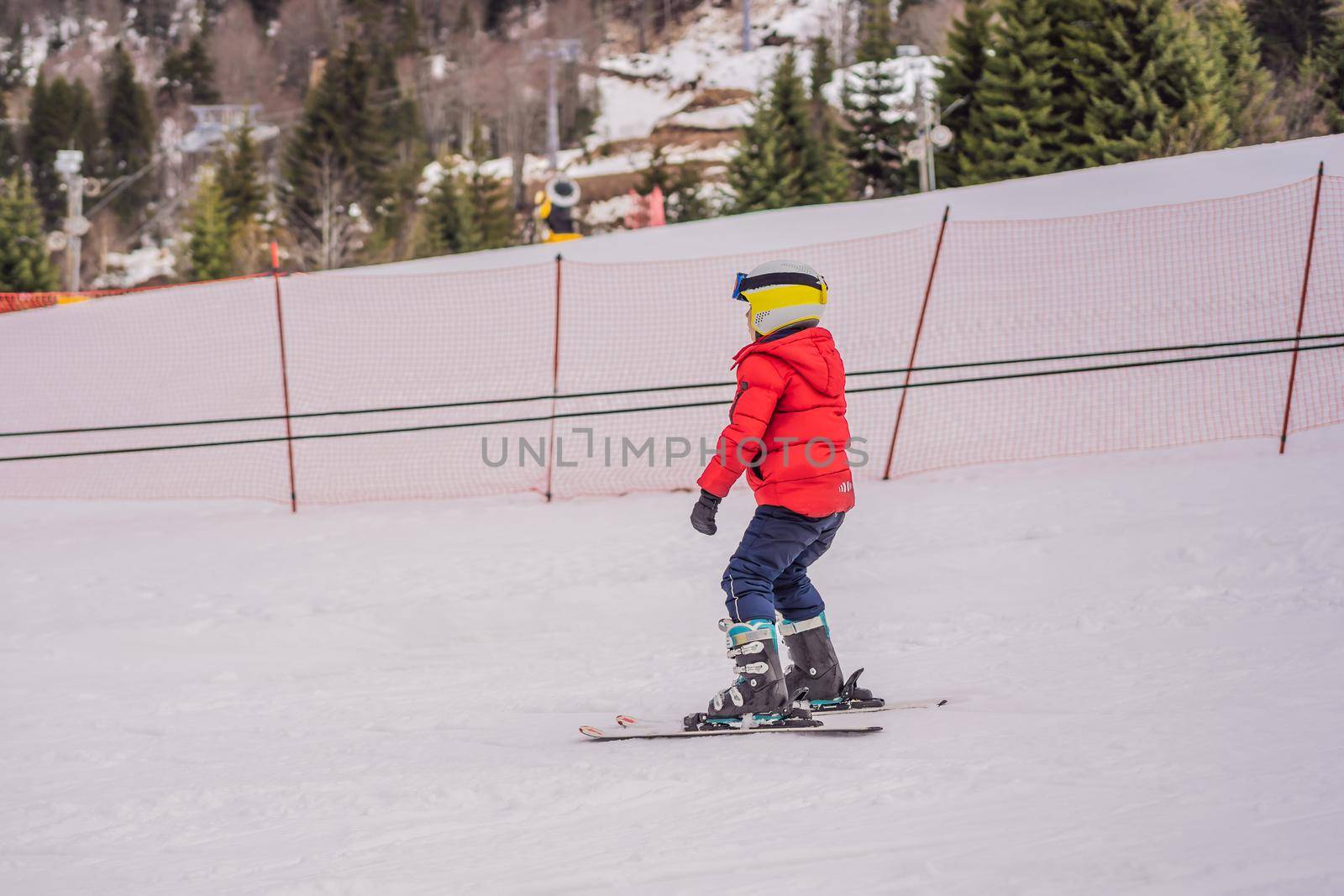 Child skiing in mountains. Active toddler kid with safety helmet, goggles and poles. Ski race for young children. Winter sport for family. Kids ski lesson in alpine school. Little skier racing in snow by galitskaya