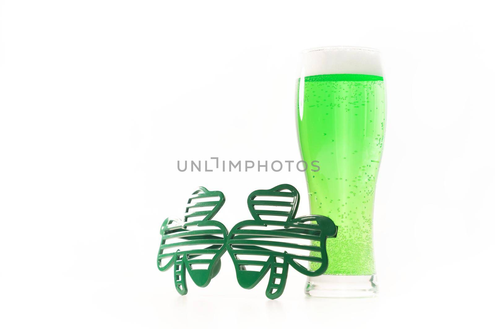 A glass of green beer and funny glasses for st patrick's day on a white background. Traditional Irish drink for a holiday. Copy spase