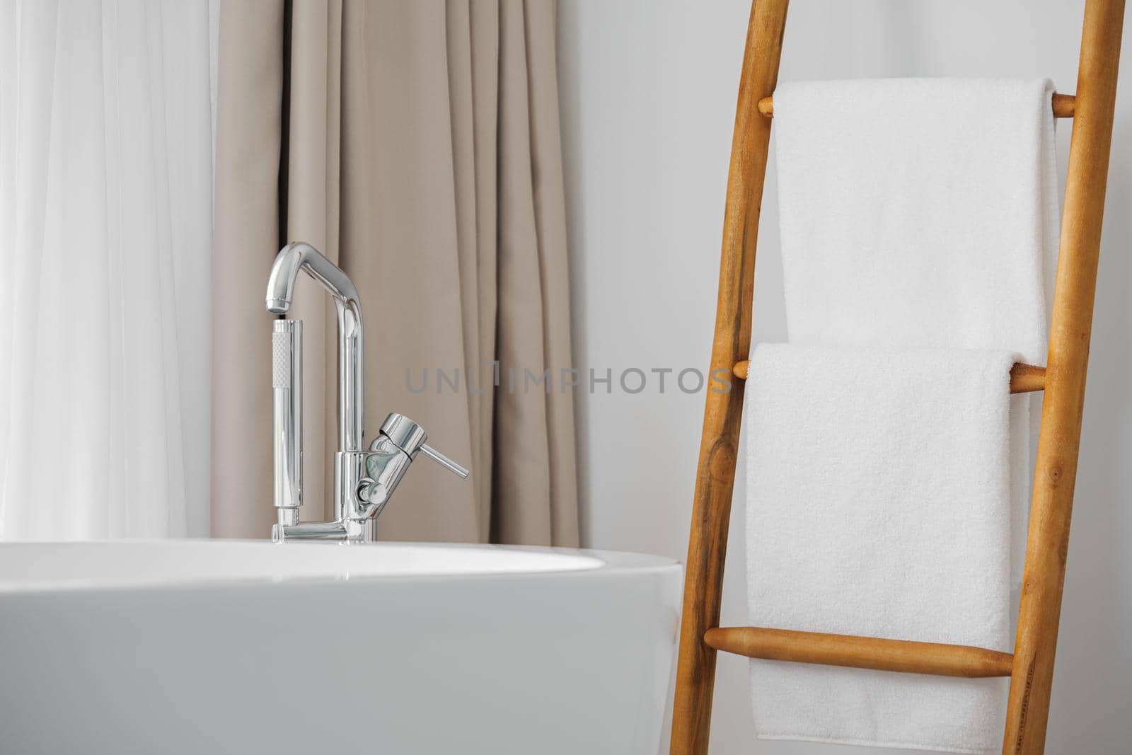 Contemporary bathroom with modern bath, metal faucet and white towels on decorative wooden stairs