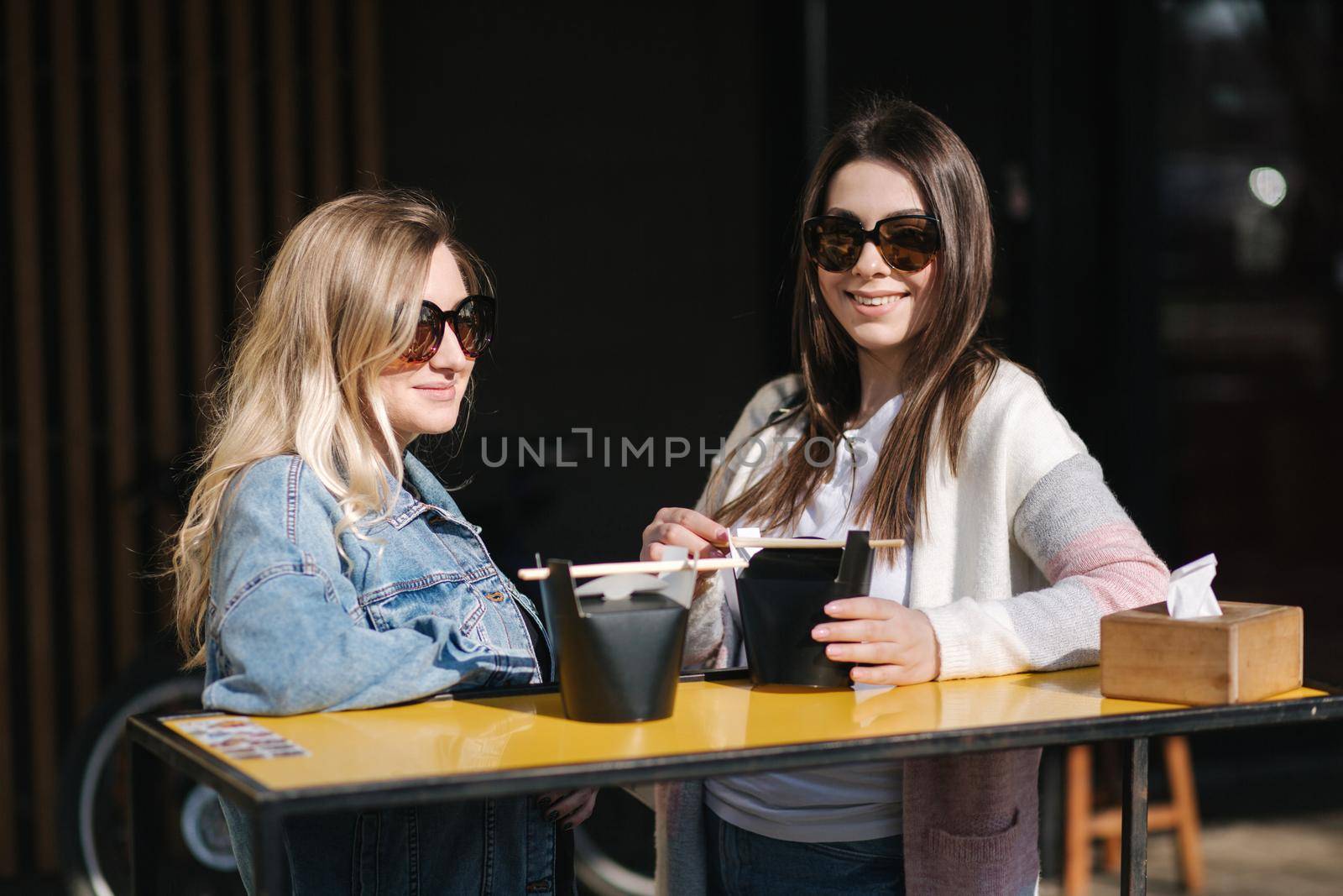 Two beautiful blonde and brunette girls order takeaway chinese food. Young woman outdoors speaking. Spring sunny day.
