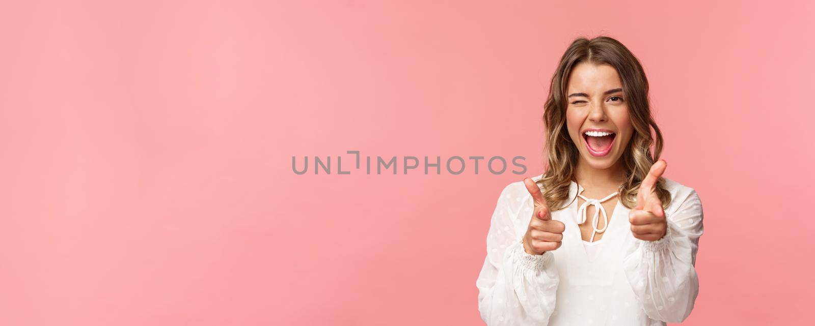 Close-up portrait of sassy and carefree good-looking emotive blond girl, pointing finger pistols at camera as asking join her team, become member, inviting try product yourself, smiling cheeky.