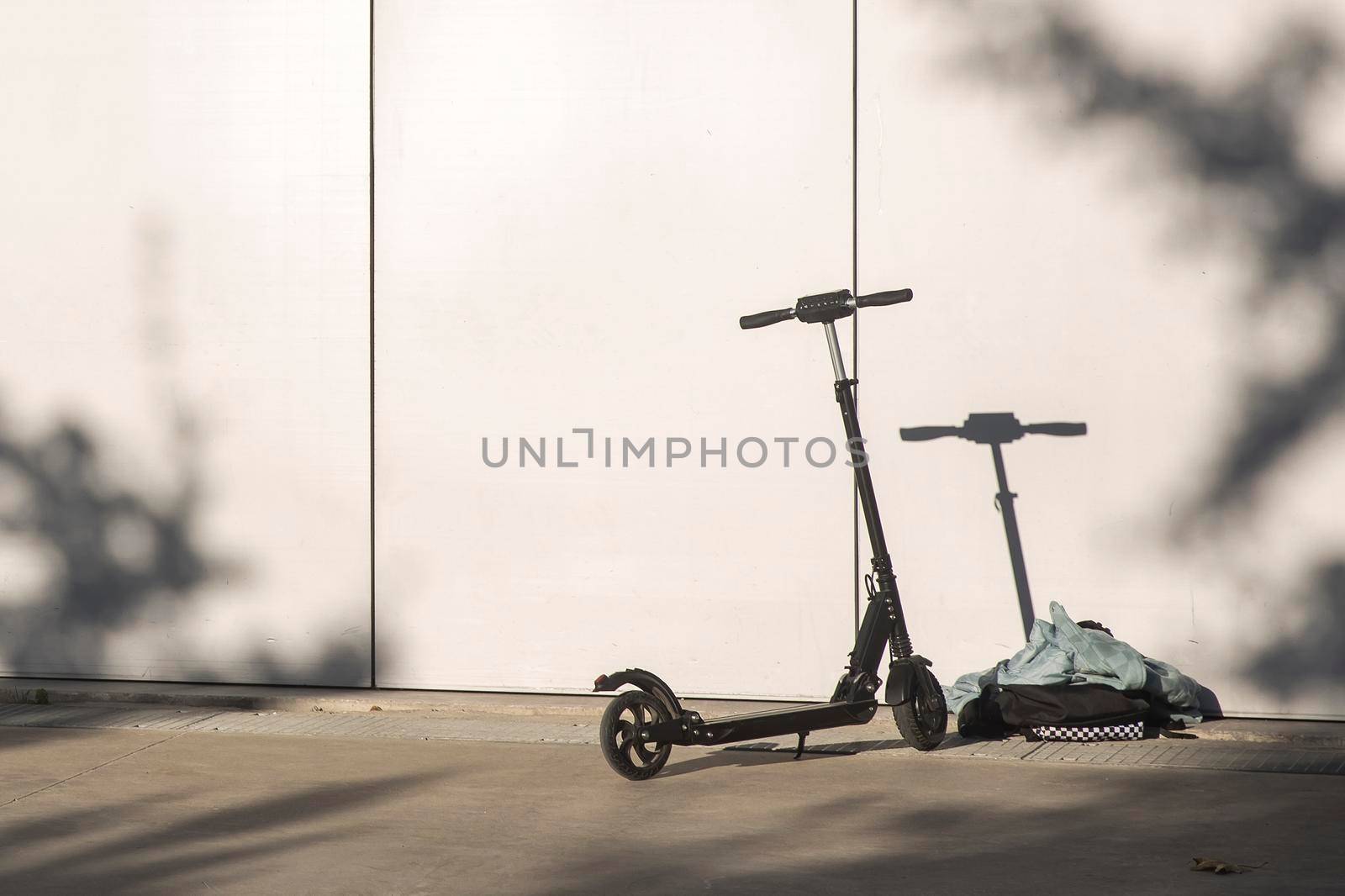 A black electric scooter is parked against the wall. The scooter casts a shadow on the wall by elenarostunova