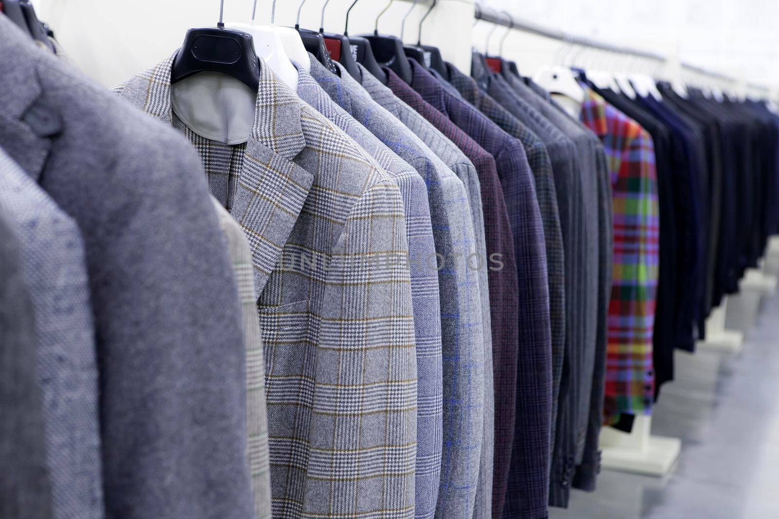 Men's tweed jackets in gray, checkered, striped hang on hangers in the store. Business style